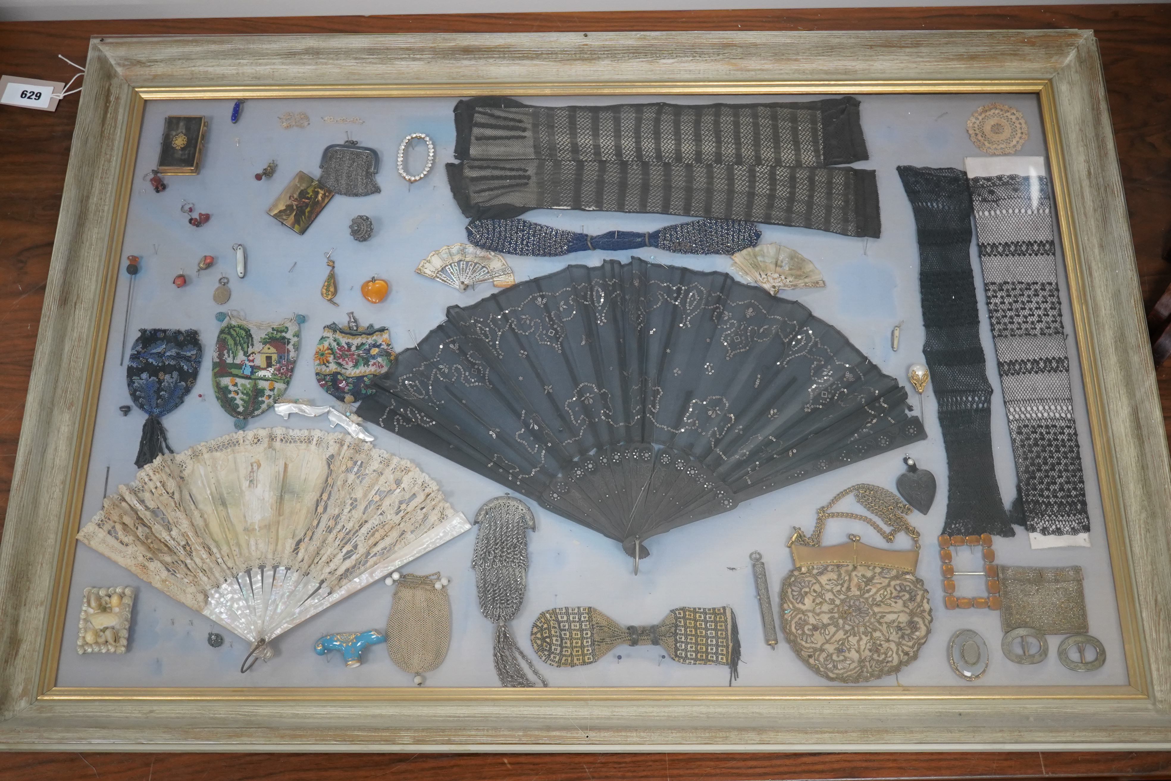 A framed display montage of late 18th and 19th century decorative ladies sequin and lace fans, beadwork reticules, cut steel misers purses, hat pins, earrings, brooches, shoe buckles and crochet mittens.100cm x 70cm. Con